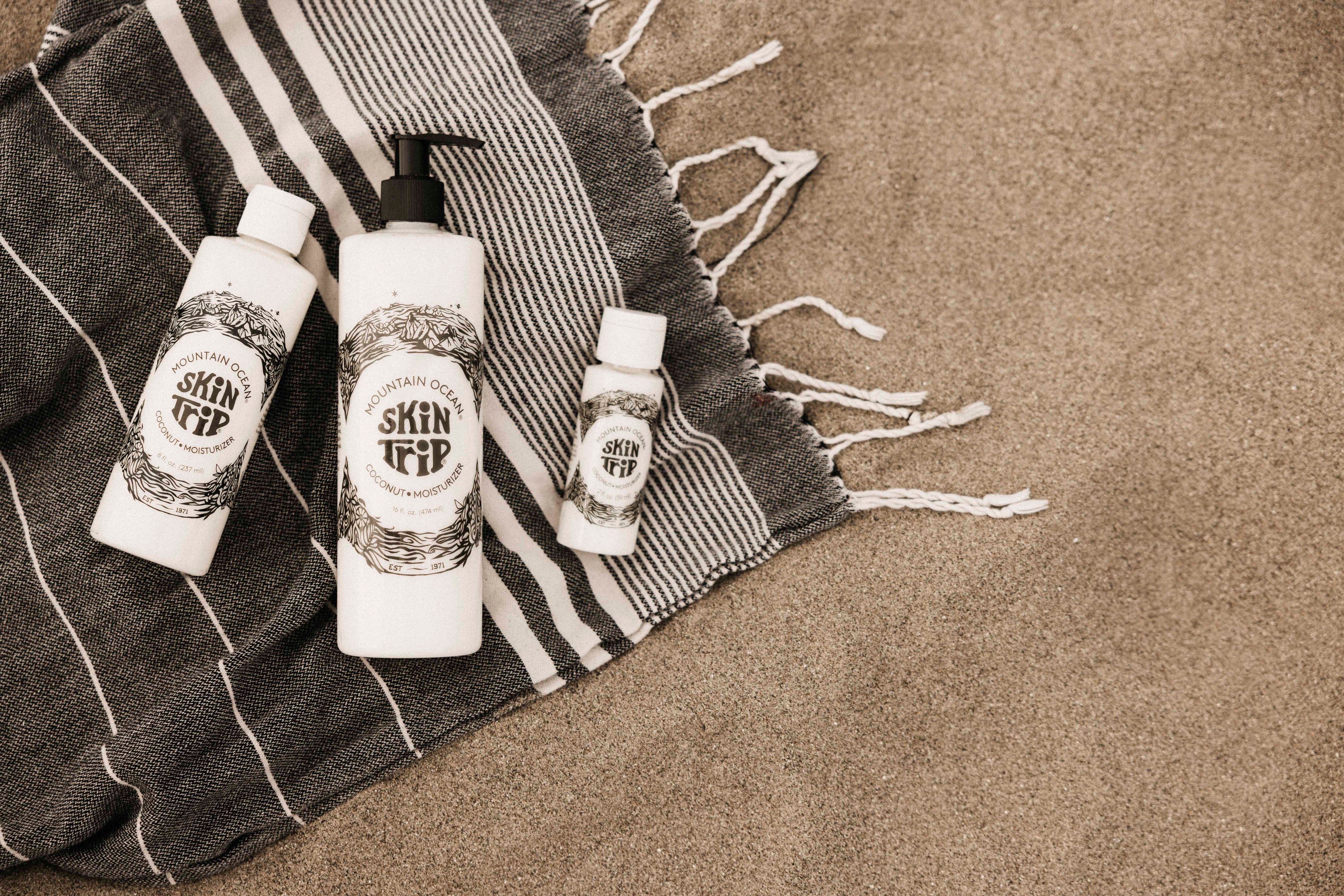 Three bottles of 'Skin Up' product on a striped towel with sand in the background