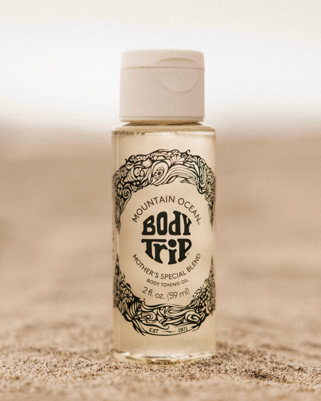 Bottle of Mountain Ocean Body Trip toning oil on a sandy background