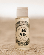 Bottle of Mountain Ocean Body Trip toning oil on a sandy background