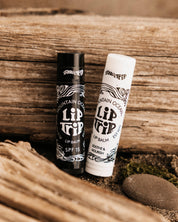 Two lip balm tubes on a wooden surface with a natural background