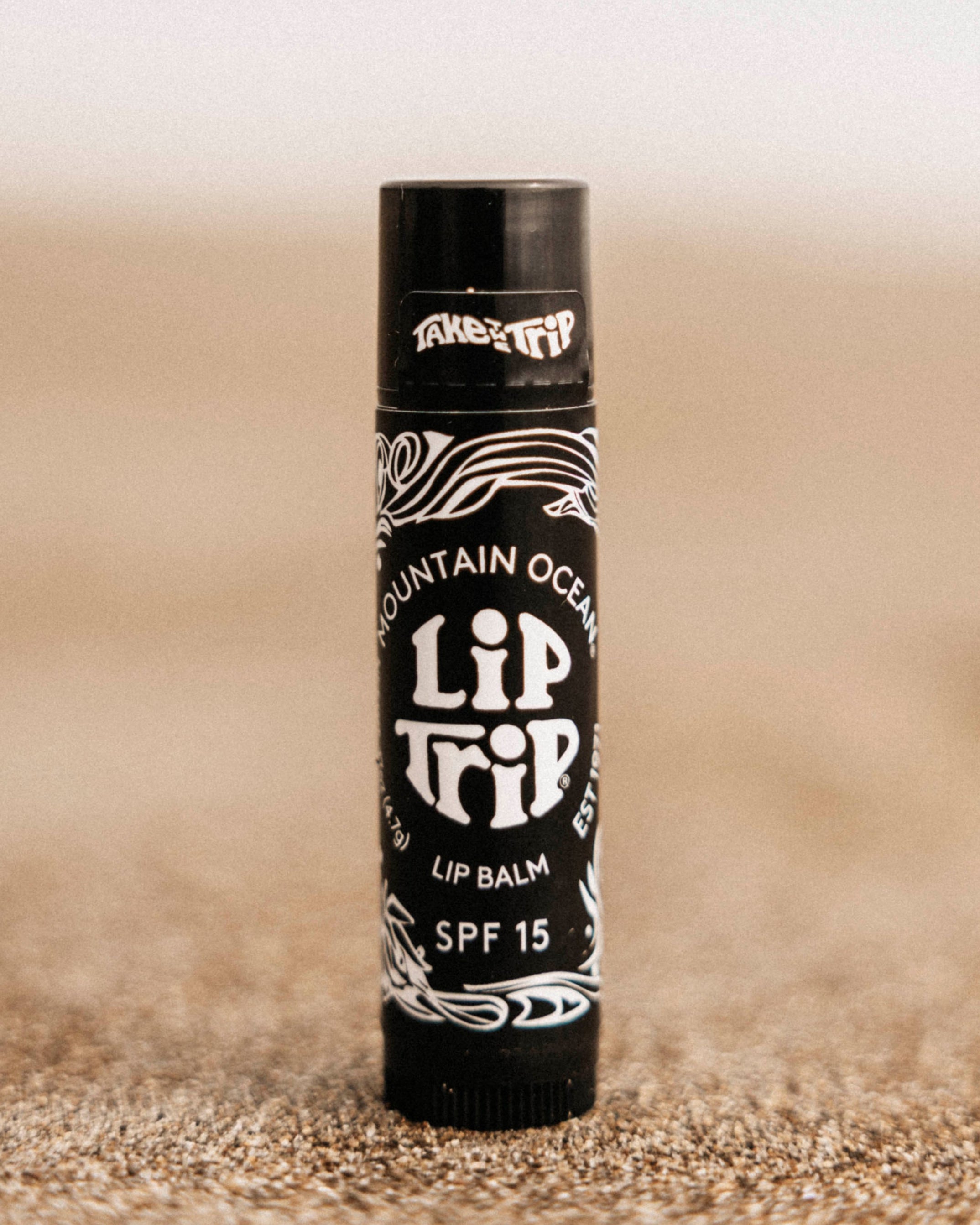 Lip balm tube labeled 'Lip It' on a sandy surface
