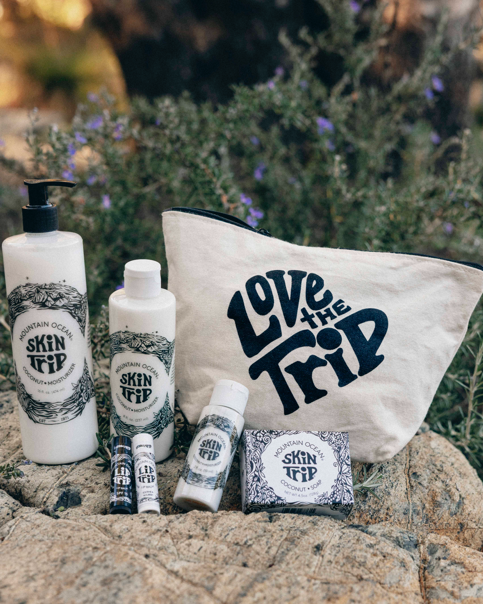 Skincare products and 'Love the Trip' bag on rocks with a natural background