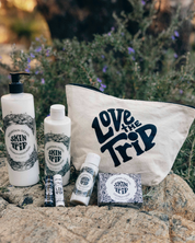 Skincare products and 'Love the Trip' bag on rocks with a natural background